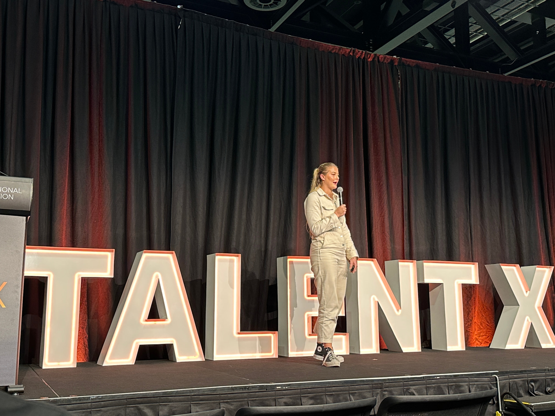 Georgia speaking on stage in front of large illuminated letters reading TALENT